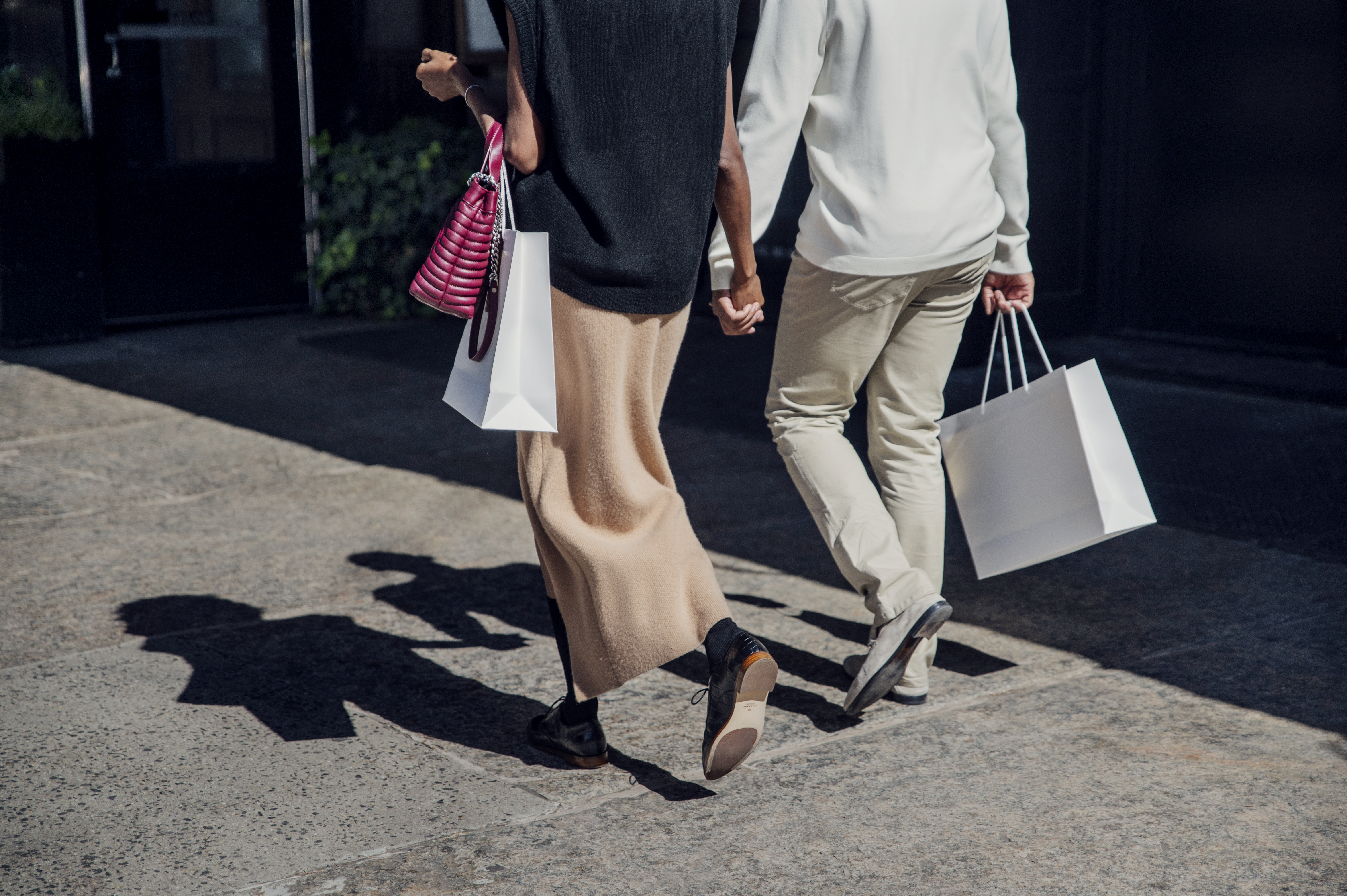 Man and woman holding hands while walking on a sidewalk with shopping bags